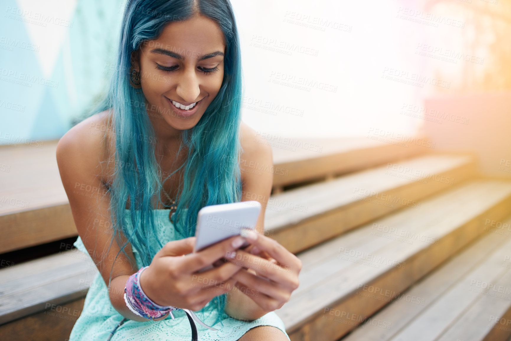 Buy stock photo Shot of a young woman sitting on the steps outside and using a mobile phone