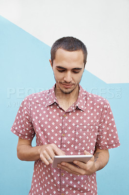 Buy stock photo Shot of a focused young student standing outside and working on his tablet before class