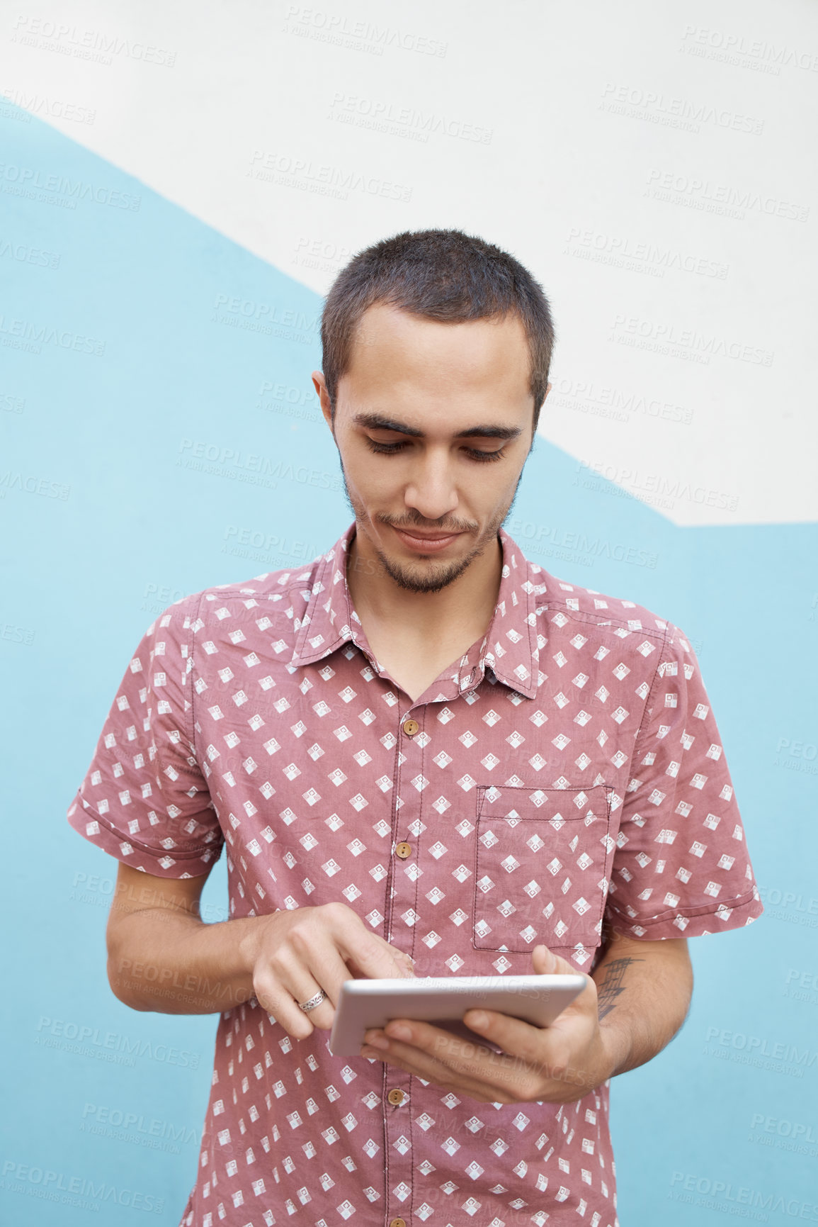 Buy stock photo Shot of a focused young student standing outside and working on his tablet before class