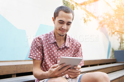 Buy stock photo Shot of a young man sitting on the steps outside and using a digital tablet