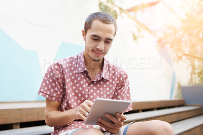 Buy stock photo Shot of a young man sitting on the steps outside and using a digital tablet