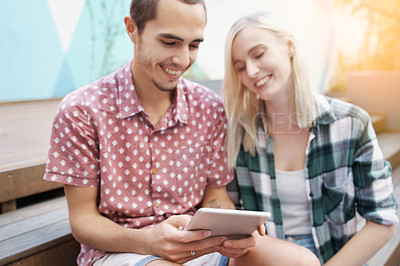 Buy stock photo Shot of a young couple sitting on the steps outside and using a digital tablet together