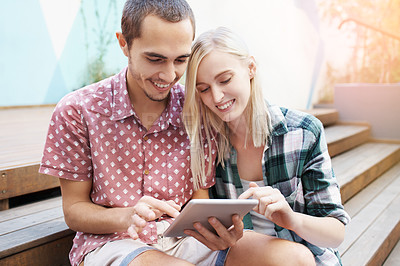 Buy stock photo Shot of a young couple sitting on the steps outside and using a digital tablet together