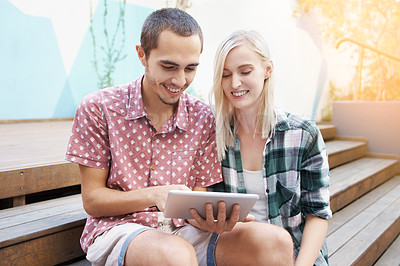 Buy stock photo Shot of a young couple sitting on the steps outside and using a digital tablet together