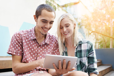 Buy stock photo Shot of a young couple sitting on the steps outside and using a digital tablet together