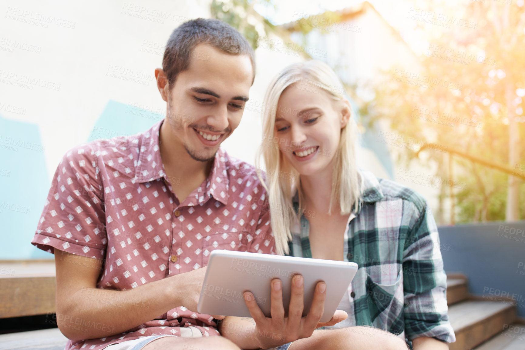 Buy stock photo Shot of a young couple sitting on the steps outside and using a digital tablet together