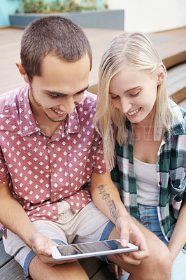 Buy stock photo Shot of a young couple sitting on the steps outside and using a digital tablet together