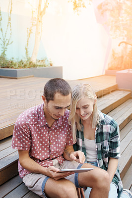 Buy stock photo Shot of a young couple sitting on the steps outside and using a digital tablet together