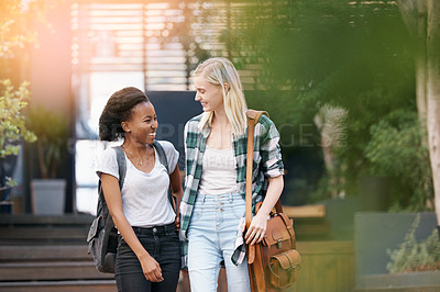 Buy stock photo Shot of two happy young friends walking together outside on campus