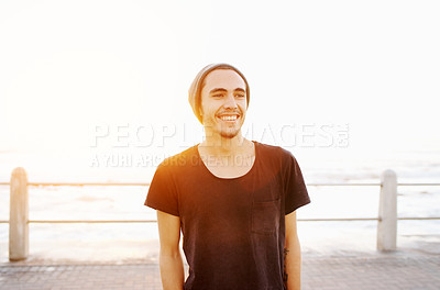 Buy stock photo Man, smile and promenade at beach in sunset with streetwear, beanie and vacation by ocean. Person, outdoor and happy by sea, waves and boardwalk on holiday with nature, sunshine and thinking in Italy