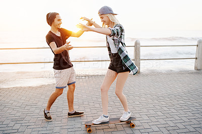 Buy stock photo Couple, skateboard and outdoor on promenade, happy and helping hand for balance, learning and playful by sea. Man, woman and teaching for skating, support and fun on boardwalk for vacation in Italy
