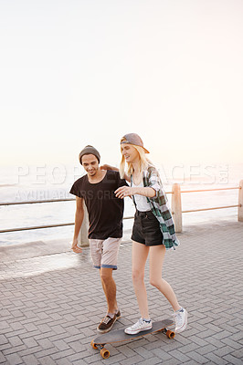 Buy stock photo Couple, skateboard and outdoor on boardwalk, happy and helping hand for balance, learning and playful by sea. Man, woman and teaching for skating, support and fun on promenade for vacation in Italy