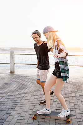 Buy stock photo Couple, man and woman with skateboard on boardwalk, happy and helping for balance, learning and playful by sea. People, teaching and skating with support and fun on promenade for vacation in Italy