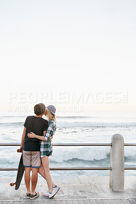 Buy stock photo Couple, kiss and romance on beach for date with mockup space, adventure and skateboard on promenade. Skater, people and hugging on boardwalk for bonding, embrace and outdoor travel with sea waves