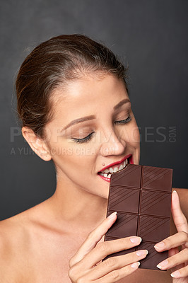 Buy stock photo Chocolate, bite and woman in studio eating for unhealthy diet, sugar craving or cheat day on dark background. Dessert, delicious and female model for snack temptation, sweet addiction or cocoa bar