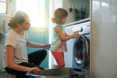 Buy stock photo Shot of a mother and daughter using a washing machine