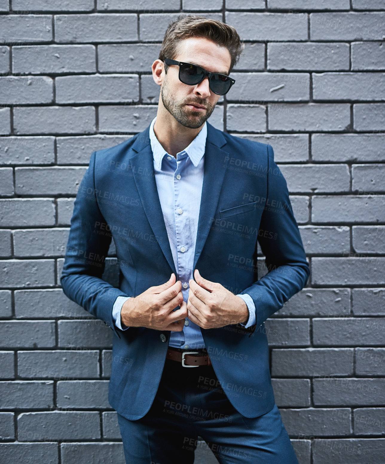 Buy stock photo Shot of a handsome young businessman standing against a grey facebrick wall