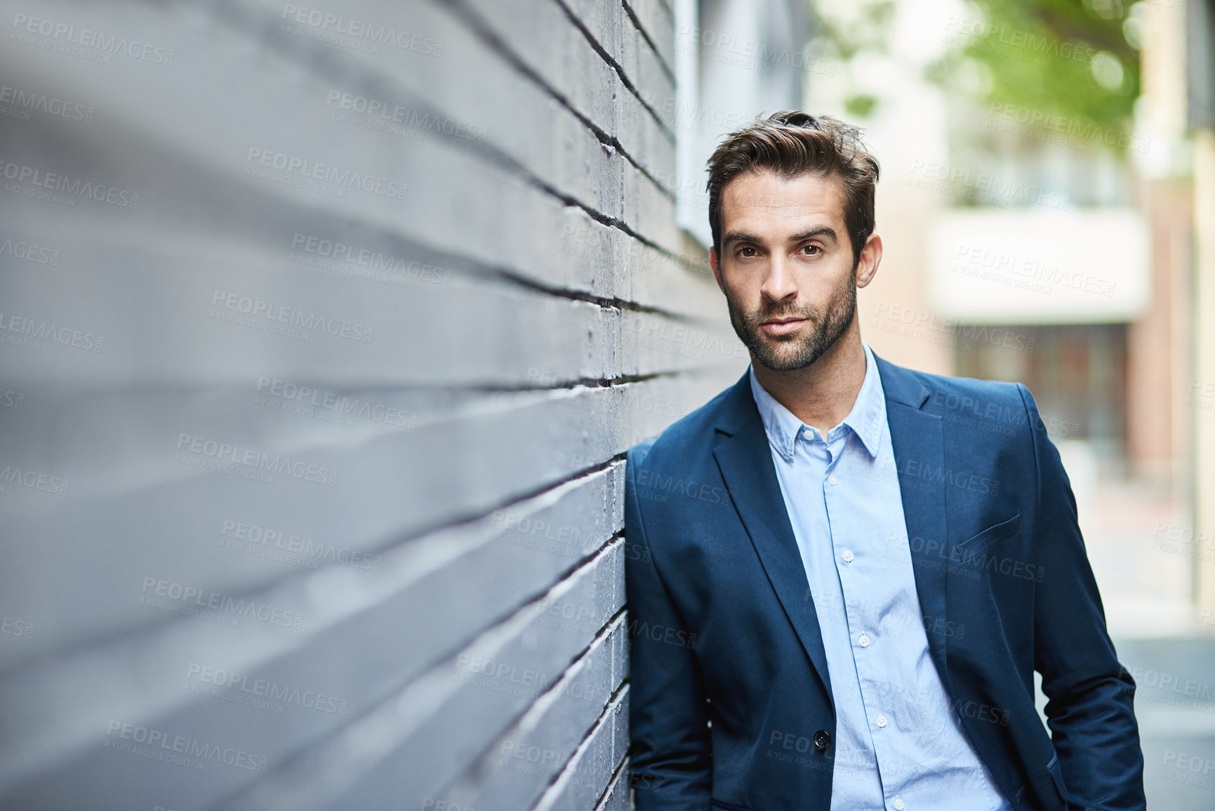 Buy stock photo Shot of a handsome young businessman standing against a grey facebrick wall