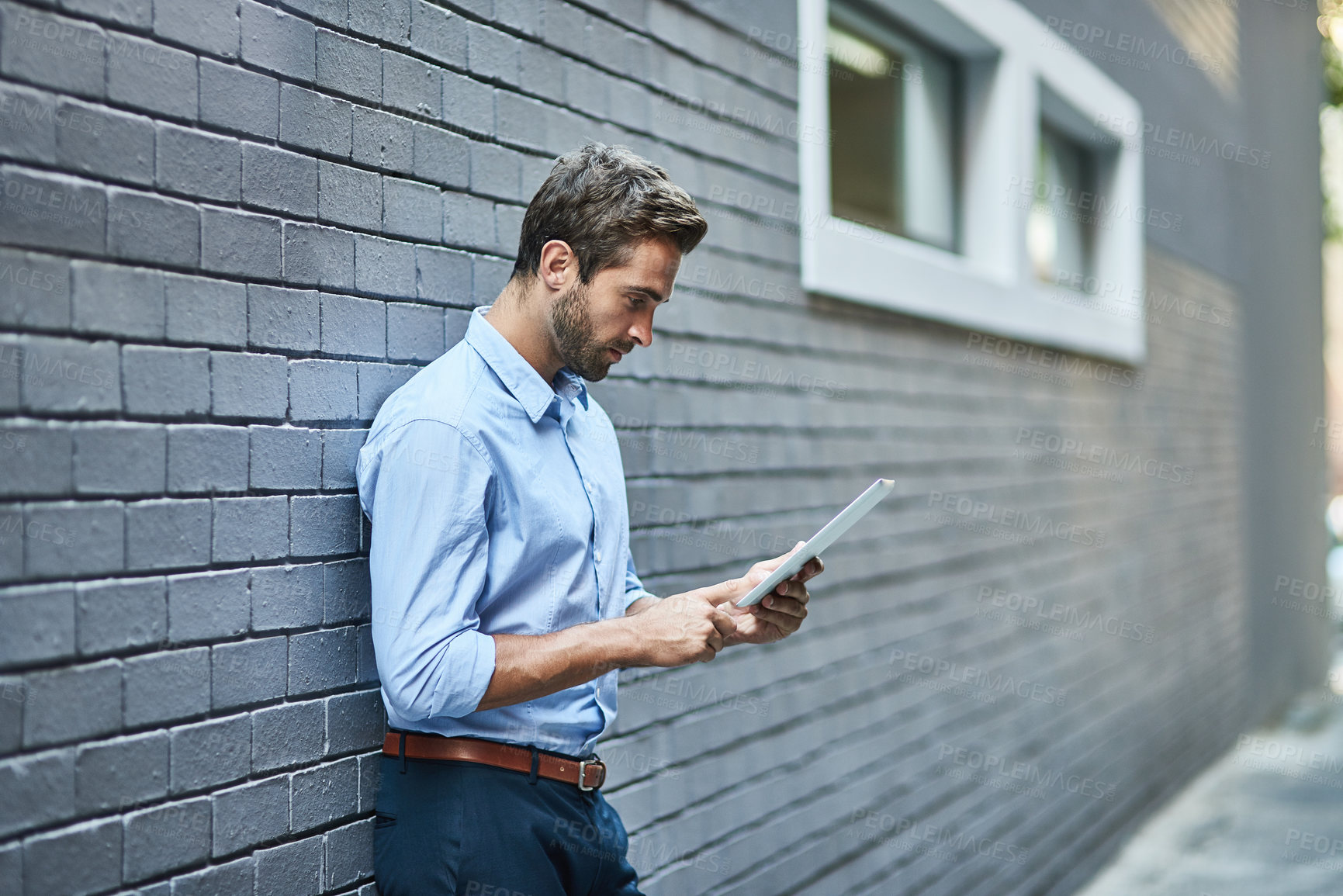 Buy stock photo Business man, tablet and research, reading email or info online on a wall in city. Serious, digital technology and professional on website, app or consultant networking on internet outdoor in town