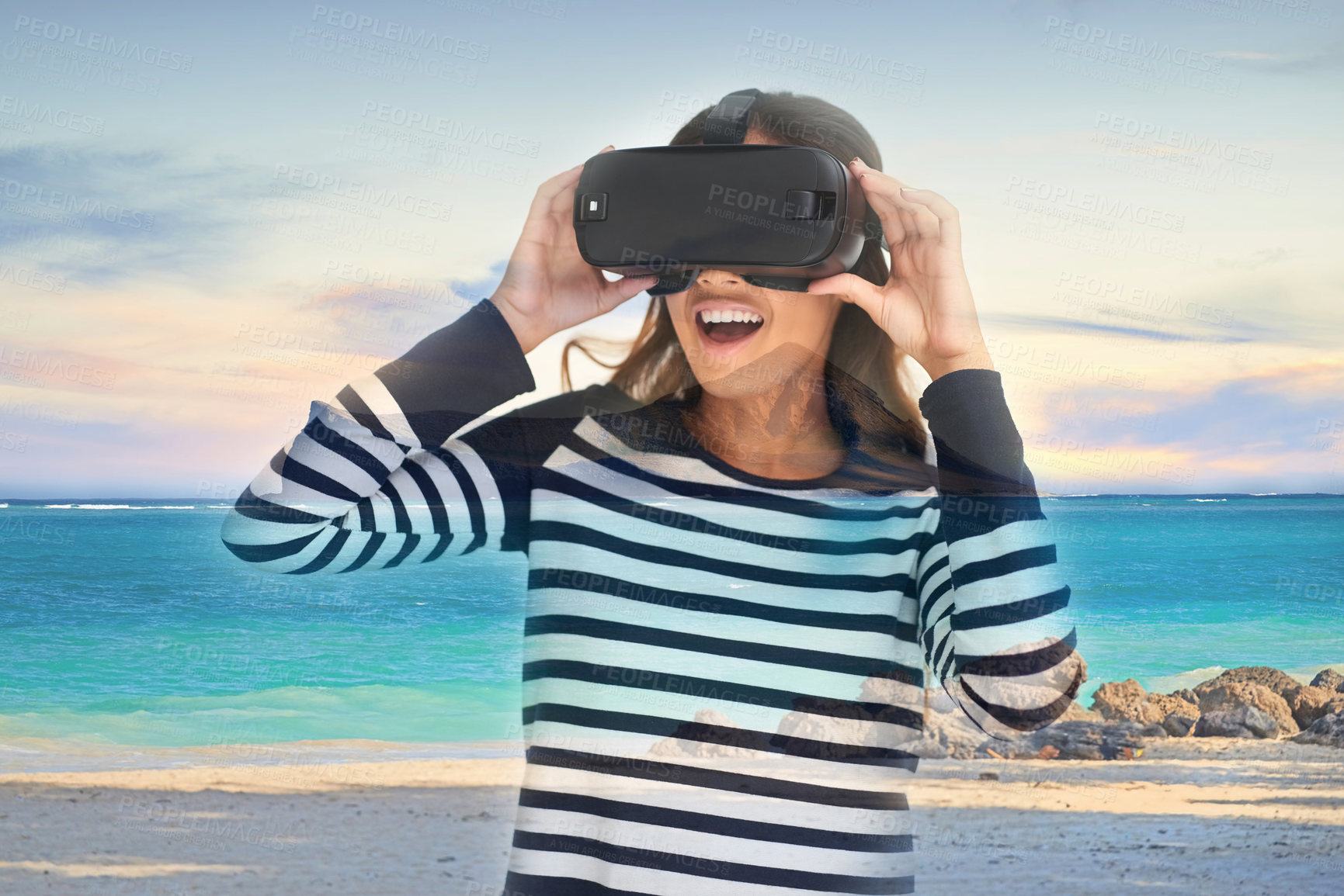 Buy stock photo Shot of a young woman wearing a VR headset superimposed over a beach landscape