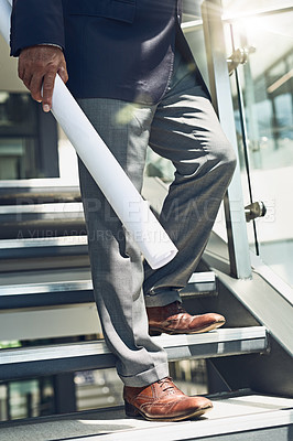 Buy stock photo Shot of a unrecognisable businessman holding blueprints while walking down stairs inside of a building