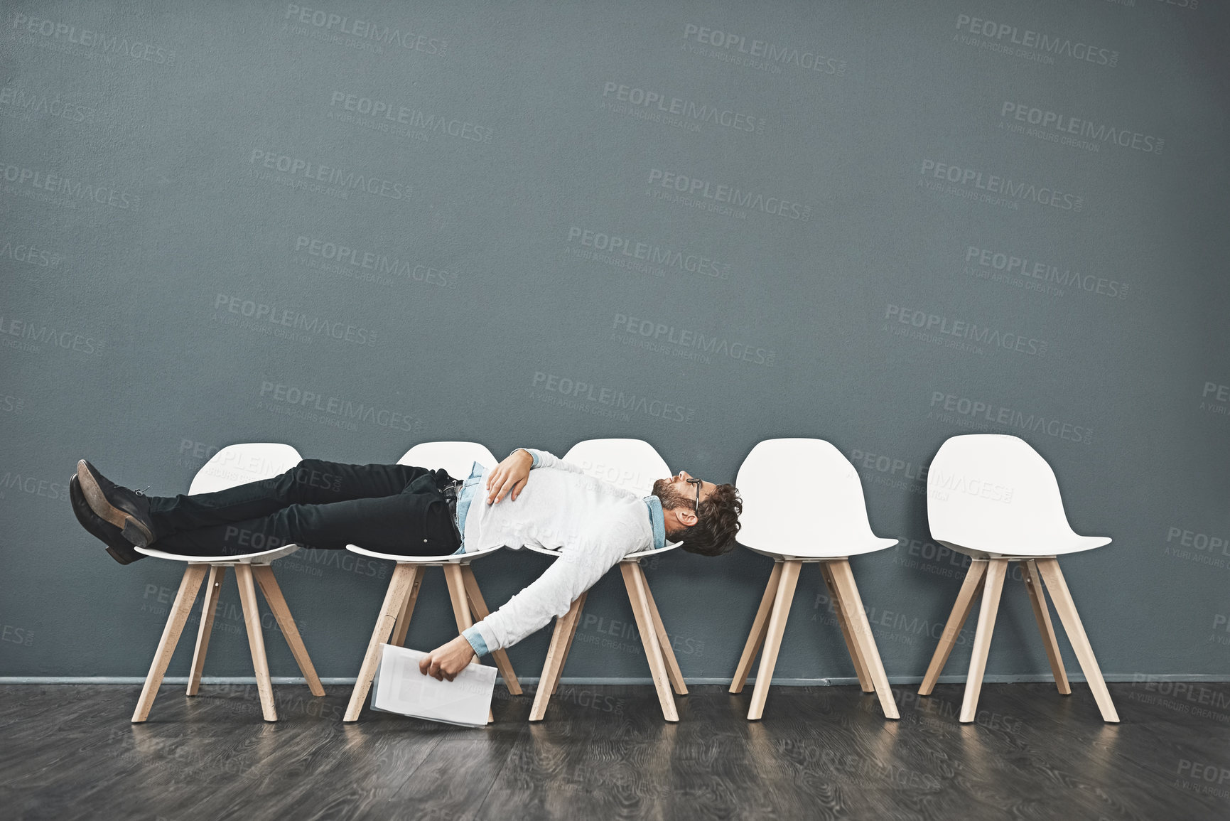 Buy stock photo Shot of a young man lying down on a row of chairs while waiting in line for a job interview