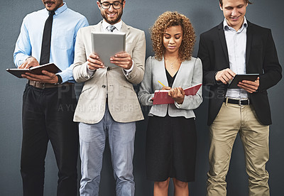 Buy stock photo Shot of a group of businesspeople using digital tablets and notebooks while waiting in line for a job interview