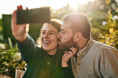 Buy stock photo Love, couple and selfie on a patio by happy people kiss, bond and relax at sunset together. Family, phone and man kissing woman for picture while sitting in a backyard, smile and loving at home