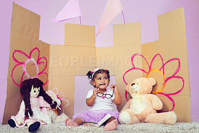 Buy stock photo Shot of an adorable little girl reading a book surrounded by her toys