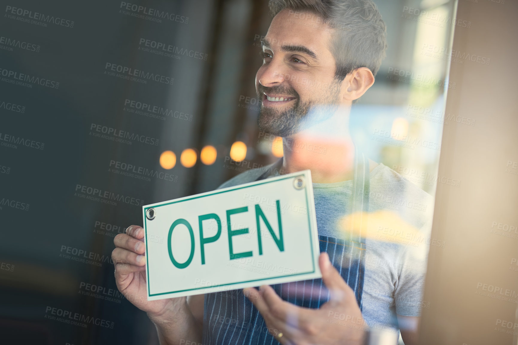 Buy stock photo Shot of a handsome young man hanging up an open sign on the door of his store
