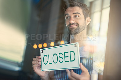 Buy stock photo Shot of a handsome young man hanging up a closed sign on the door of his store