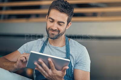 Buy stock photo Shot of a young man using a digital tablet while working at a coffee shop