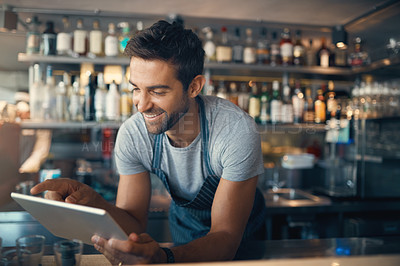 Buy stock photo Shot of a young man using a digital tablet while working behind a bar counter