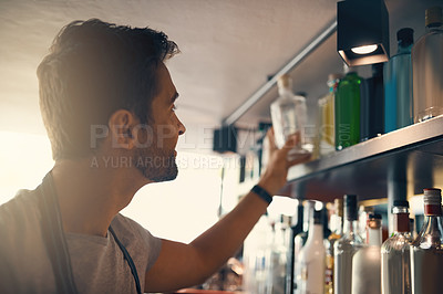 Buy stock photo Shot of a young man looking at the merchandise on the shelves behind a bar counter