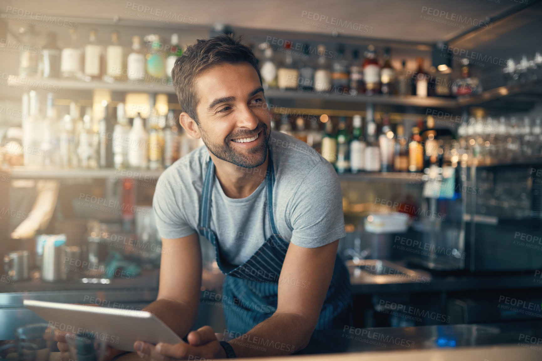 Buy stock photo Shot of a young man using a digital tablet while working behind a bar counter