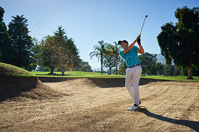 Buy stock photo Shot of a focused young man hitting a golfball out of a sandbank on a golf course outside