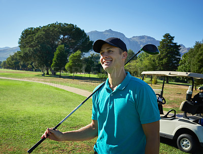 Buy stock photo Shot of a cheerful young man holding a golf club and looking into the distance while standing on a golf course outside