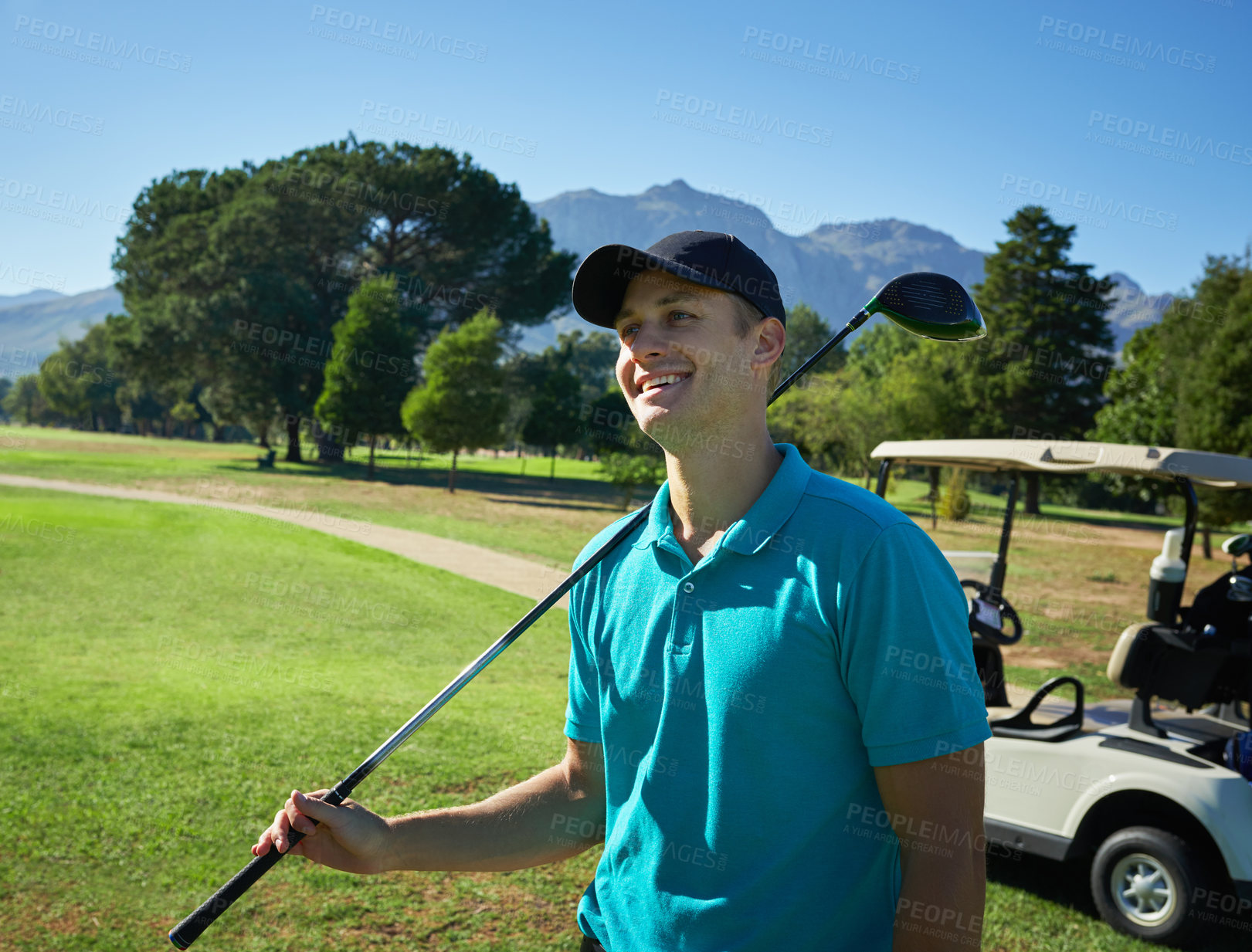 Buy stock photo Shot of a cheerful young man holding a golf club and looking into the distance while standing on a golf course outside