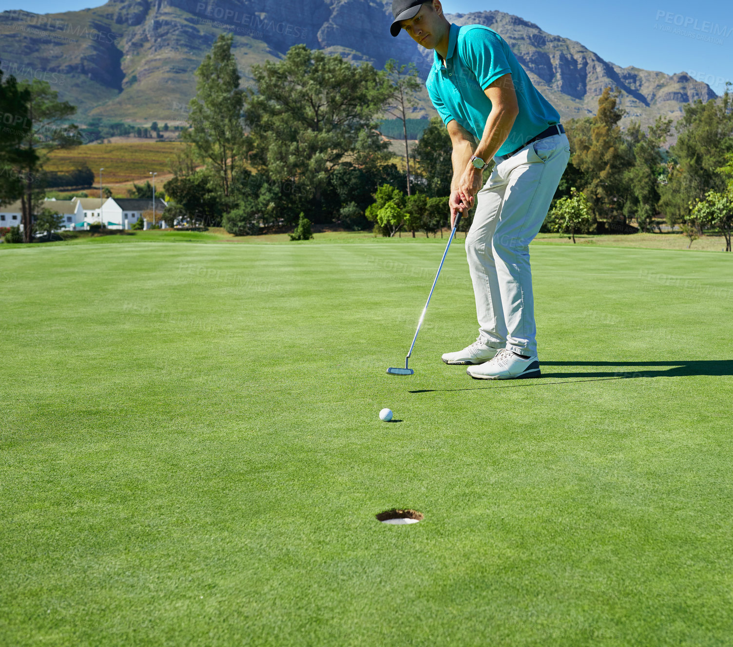 Buy stock photo Shot of a focused young man hitting a golfball with a putter into a hole on a golf course