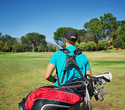 Buy stock photo Shot of a unrecognizable young man walking with his golf gear outside on a golf course