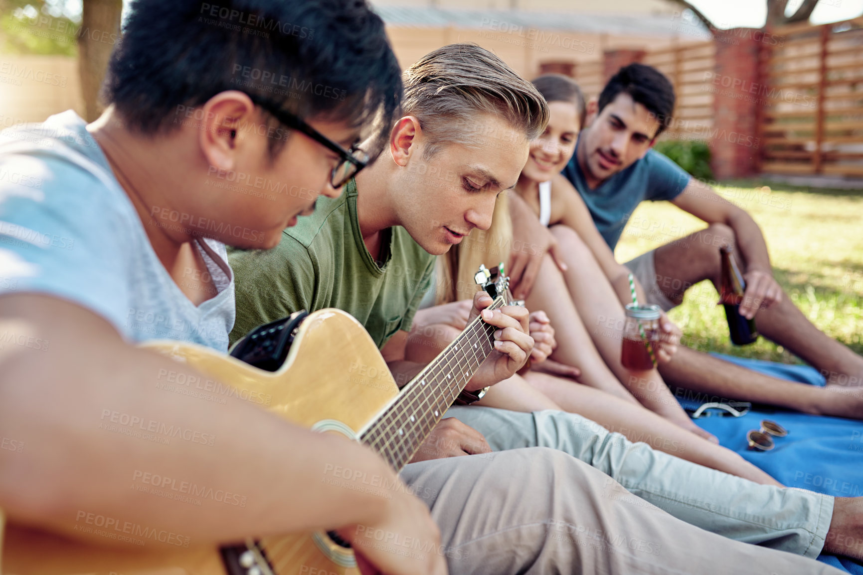 Buy stock photo Cropped shot of a young man playing guitar while enjoying a few drinks with his friends outside in the summer sun