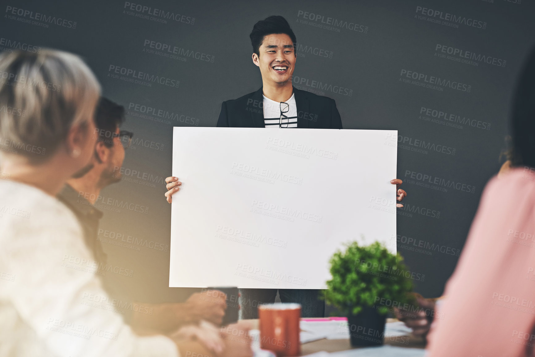 Buy stock photo Shot of a young businessman holding up a placard during a meeting inside