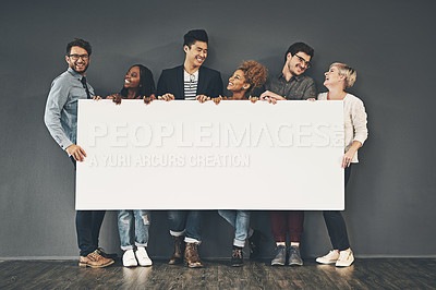 Buy stock photo A copyspace of a diverse group of young, happy and smiling professional business people holding a blank white billboard. A multiracial team of men and women against a dark wall with copy space 