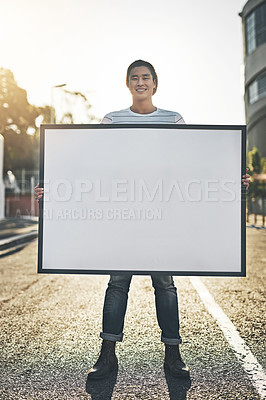 Buy stock photo Young man holding an empty sign, board or placard while standing outside in the city street. Portrait of one happy, smiling and cheerful guy making an annoucement, showing an ad or doing promotion
