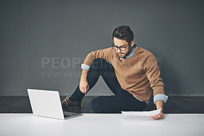 Buy stock photo Business man working on a laptop, reading a report and going through finance paperwork while sitting on the floor in an office at work. Serious professional manager looking at papers with copyspace