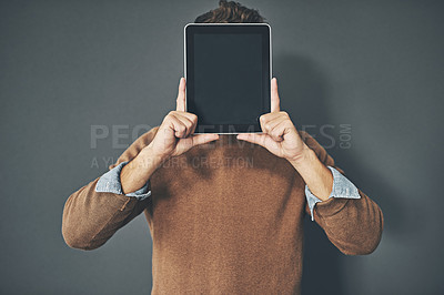 Buy stock photo Young man holding a blank tablet up to his face, in casual wear against a gray background with copy space. Alone male standing with a blank screen pressed against his head. Adult posing with a device
