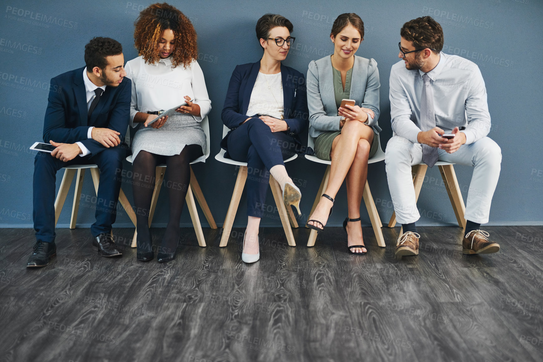 Buy stock photo Group of business people networking on phones, digital tablets and social media, waiting in line. Diverse team of colleagues sitting in queue, talking and discussing against blue copyspace wall.