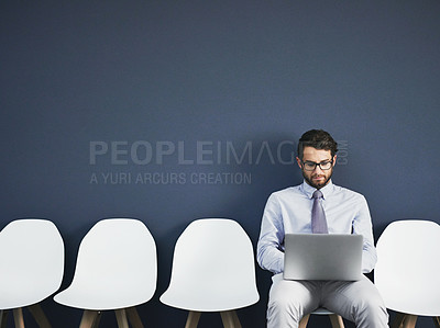 Buy stock photo Studio shot of a young businessman using a laptop while waiting in line against a gray background