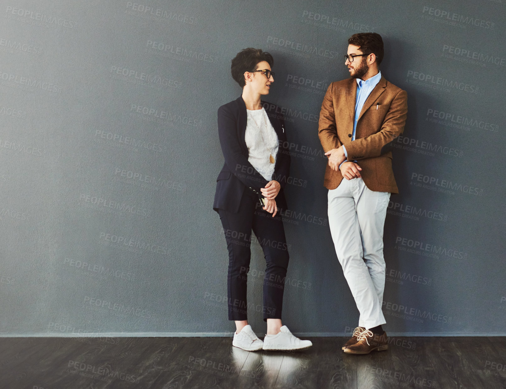 Buy stock photo Shot of two designers having a conversation while leaning against a wall