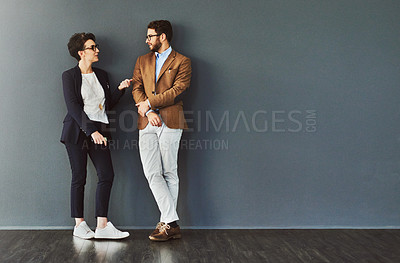 Buy stock photo Shot of two designers having a conversation while leaning against a wall